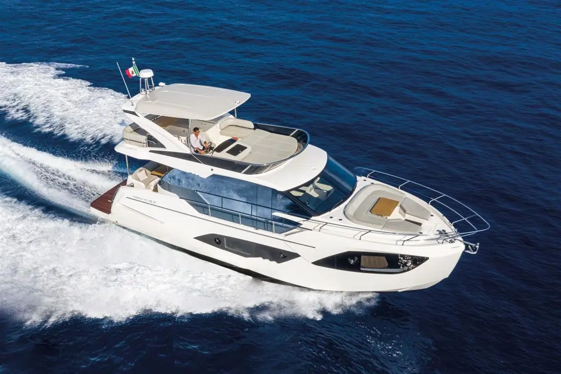 Luxury motor yacht cruising through blue waters with a man at the helm, featuring elegant exterior design and sleek lines.